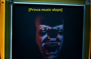 Cain's computerized face on his new Robocop body display; he is mad. Caption reads "Prince Music Stops."
