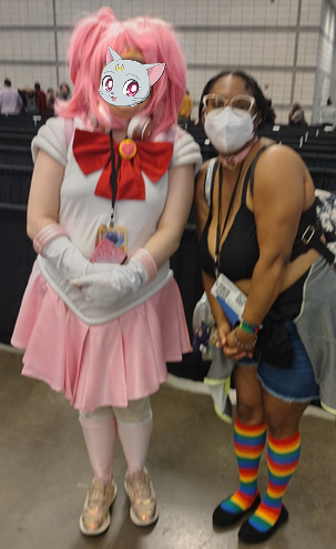 Me and a Chibiusa cosplay standing side-by-side, smiling. (I'm wearing a N95 mask while their face is covered with a emoji sticker of Diana, the grey kitten from Sailor Moon.)
