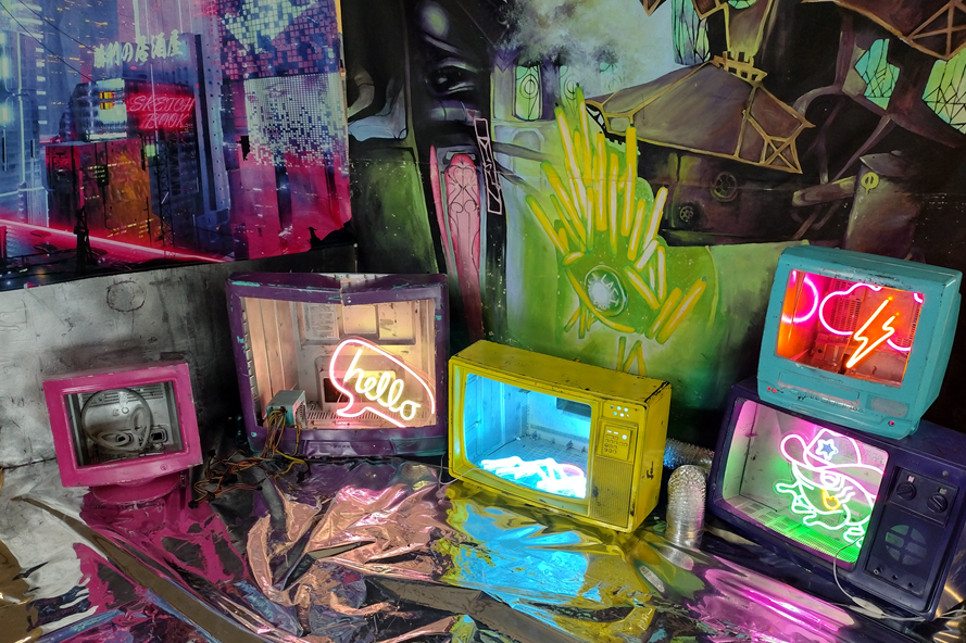 A cyberpunkish photoshoot space, with neon lights and various retro TVs and CRT monitors in loud colors.