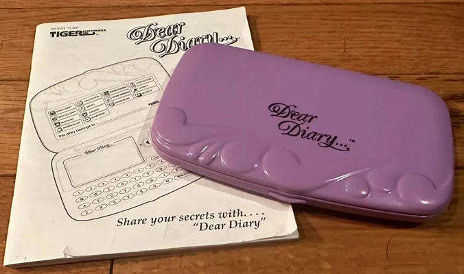 An electronic organizer , pink with "Dear Diary..." in fancy script font on its cover. The instruction manual rests below it.