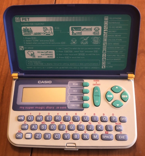 Casio's "My Super Magic Diary", open to reveal a white chassis and blue cover. The buttons are teal and purple, with dark pink for alt lettering. There is also green teal instructions in its cover.